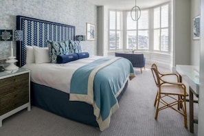 A bedroom with a large bed, a bedside table, a chair, a desk, and a window with blinds. - THE Fowey (Fowey)