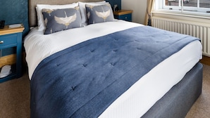 A hotel room with a large bed, a nightstand, a window with a view of the city, and a blue and white color scheme. - Ennios Boutique Hotel (Southampton)