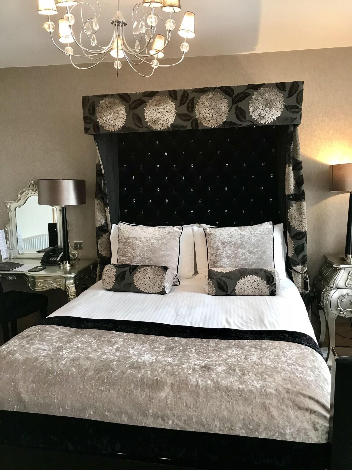 Una cama bien hecha con cabecera capitonada, un escritorio con lámpara y un candelabro.