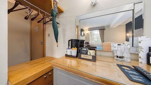 A hotel room with a wooden bench, a coffee maker, a mirror, and a minibar. - Ennios Boutique Hotel (Southampton)