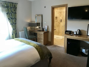 A hotel room with a bed, desk, chair, television, and a shower area. - Ennios Boutique Hotel (Southampton)