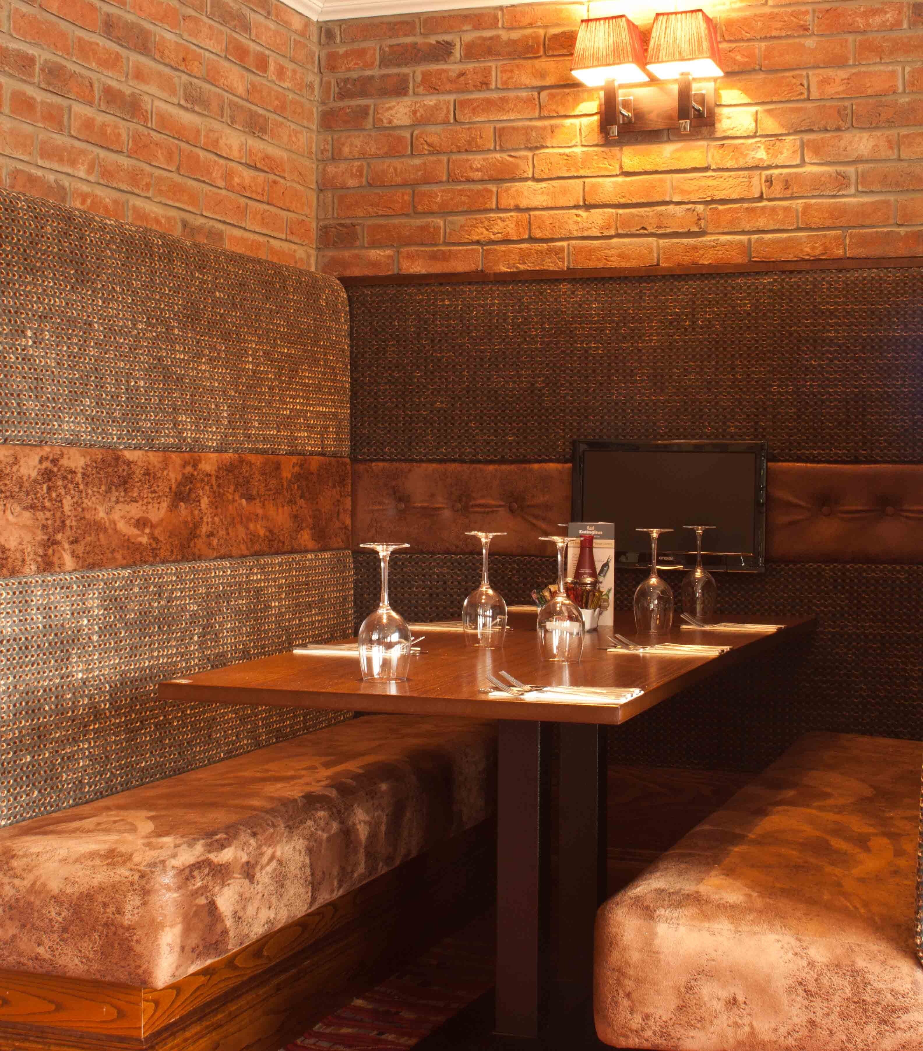 A restaurant interior with brick walls, cushioned booths, and a long table with wine glasses and cutlery.
