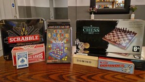 Verschiedene Gesellschaftsspiele, darunter Scrabble, ein reisespiel, ein Schachspiel, Dominosteine und Spielkarten auf einem Holztisch.