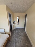 Habitación de hotel con cama, un escritorio pequeño, una silla, un bote de basura y una puerta que da a otra habitación.