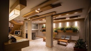 Un hall d'entrée moderne avec des poutres en bois, un comptoir d'accueil, un espace salon et des plantes en pot.