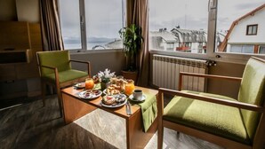 Un coin repas avec une table mise pour le petit-déjeuner, une chaise verte, une plante en pot et une vue sur les bâtiments par une fenêtre.