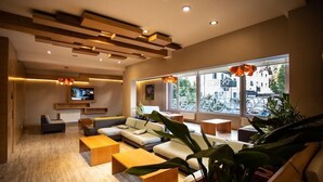 Un salon moderne avec un canapé d’angle, des tables basses en bois et de grandes fenêtres offrant une vue sur la ville.