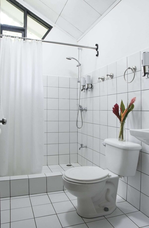 A bathroom with a shower, toilet, and a vase with flowers on the sink. - Tapirus Lodge (Guapiles)