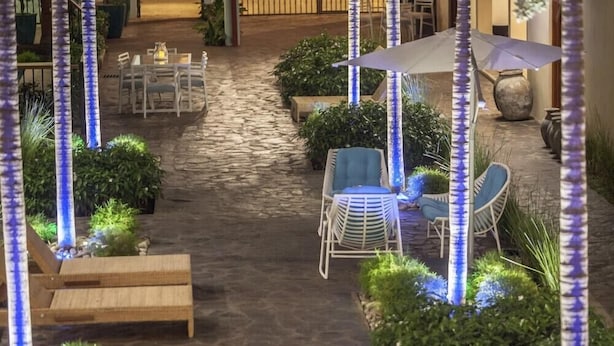 An outdoor patio area with stone flooring, white wicker furniture, and blue lighting on columns. - Paraiso Granada (Granada)
