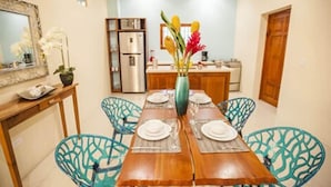 A dining area with a wooden table set for four, surrounded by blue chairs, a vase with flowers, and a kitchen in the background. - Paraiso Granada (Granada)