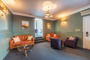 Un hall d’hôtel avec un tapis à rayures, des canapés en cuir, une table basse en verre et des appliques murales.