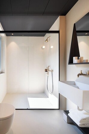 Un baño moderno con cabina de ducha de vidrio, un lavamanos blanco y un estante negro con artículos de aseo.