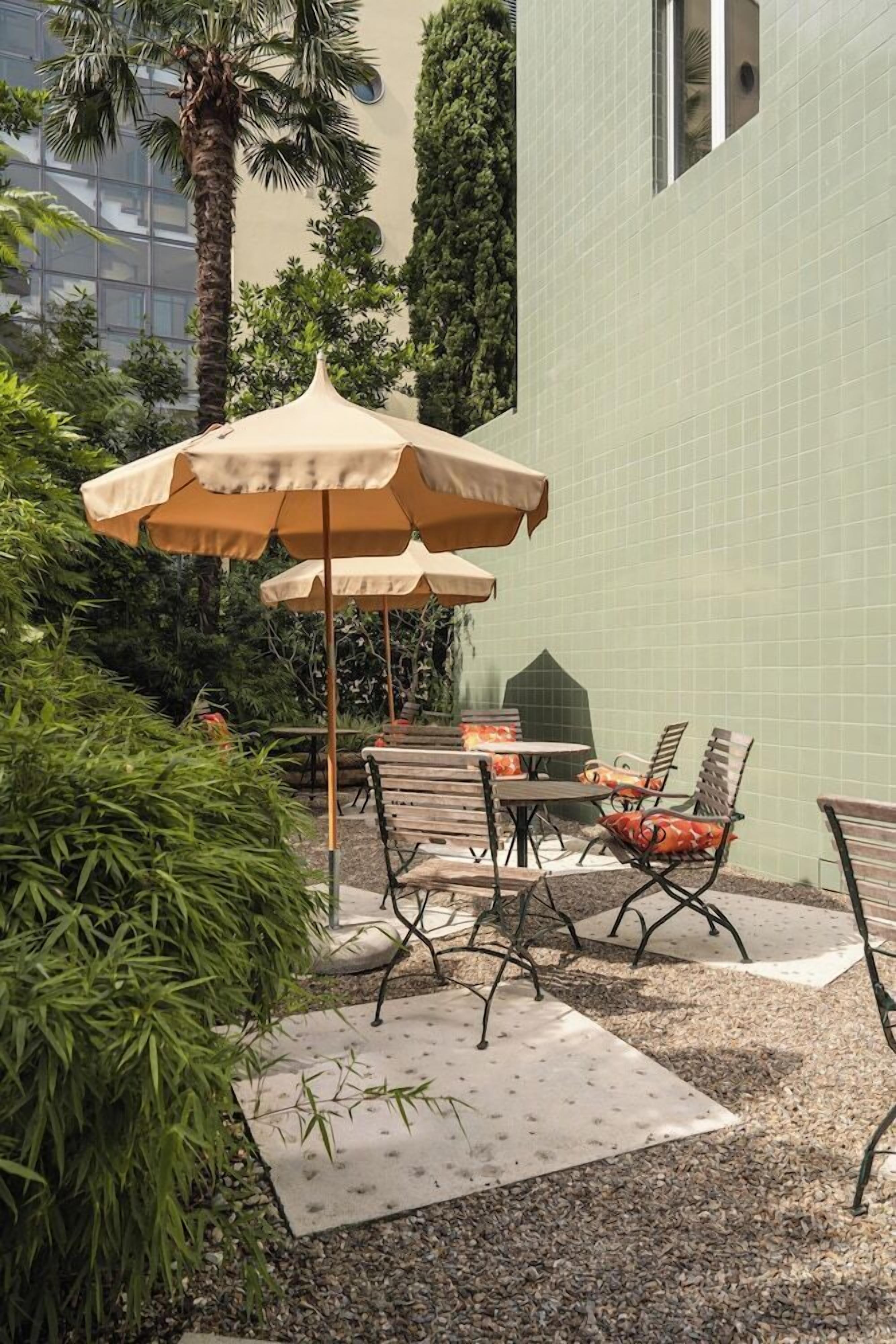 An outdoor patio area with tables and chairs, surrounded by greenery and a tiled wall.