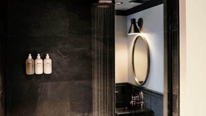 Une salle de bain moderne avec une douche à parois de verre, un grand miroir et trois flacons de produits de toilette fixés au mur.