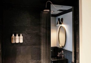 A modern bathroom with a glass-enclosed shower, a large mirror, and three bottles of toiletries on the wall. - Life House Lower Highlands (Denver)