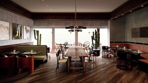 L’intérieur d’un restaurant présente un sol en bois, une table à manger centrale, plusieurs chaises et des cactus utilisés comme éléments de décoration.