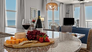 Een hotelkamer met een eethoek, voorzien van een marmeren aanrecht, een fles wijn, een glas wijn, kaas, druiven en aardbeien.