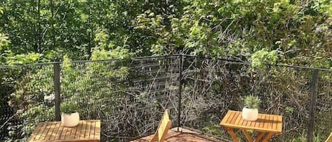 An outdoor patio with wooden tables and chairs, surrounded by a fence and dense foliage.