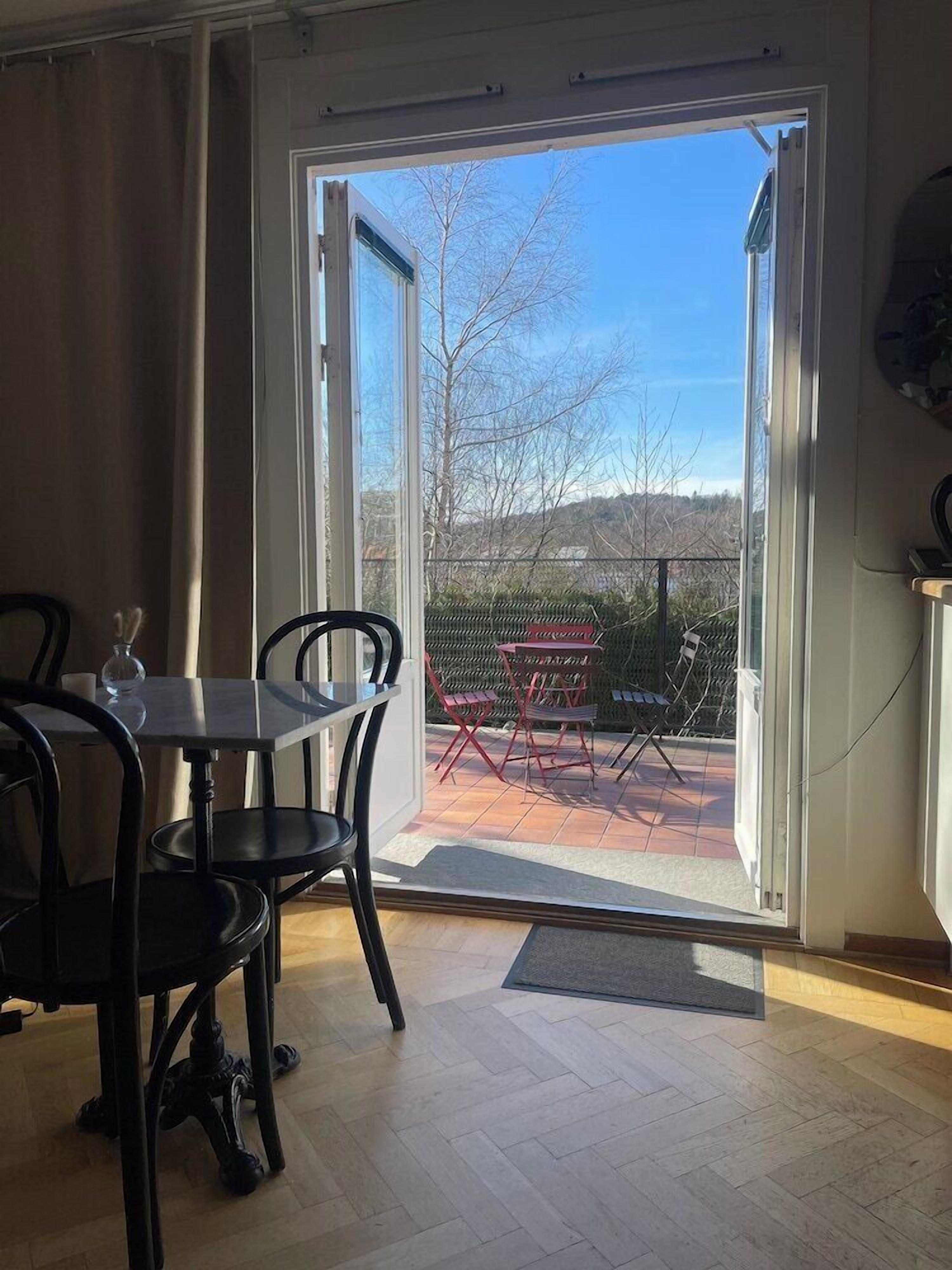 A room with a dining table and chairs, a sliding glass door leading to an outdoor patio with a red chair and a table.
