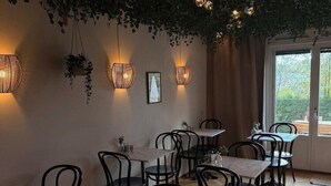 Een restaurant interieur met houten tafels en stoelen, hangende planten en wandlampen.