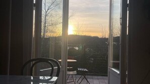 Een open schuifdeur die uitkomt op een terras met een tafel en stoelen, en uitzicht op de ondergaande zon.