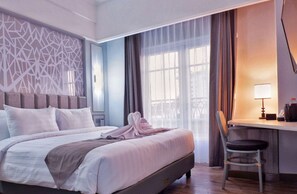 Une chambre d’hôtel avec un lit, un bureau, une chaise et une fenêtre avec des rideaux.