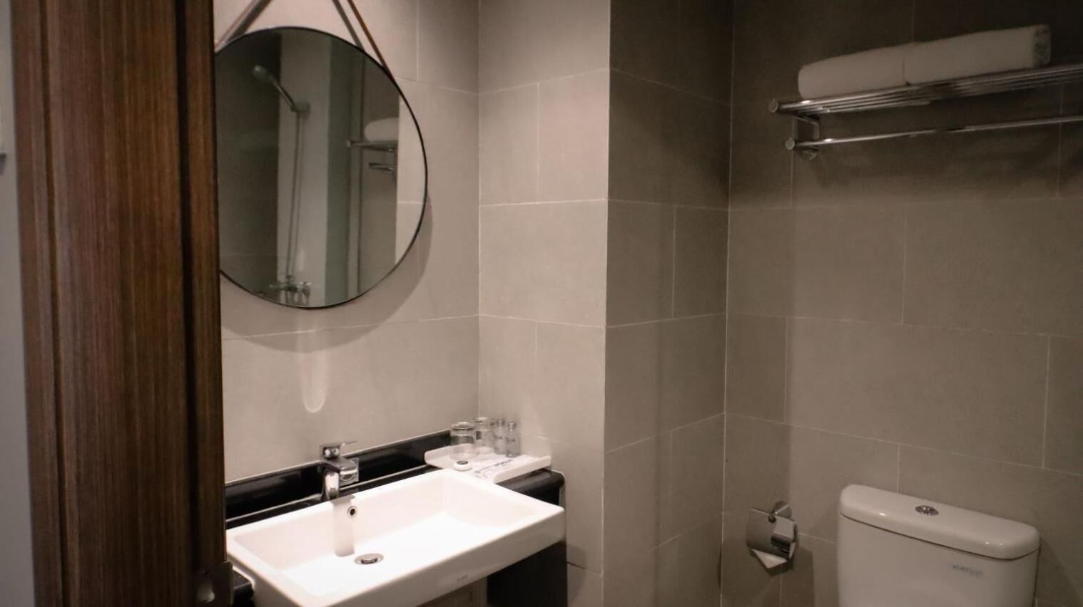 Un baño con un lavabo blanco, un espejo redondo, un inodoro y un perchero para toallas.