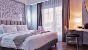 A hotel room with a bed, a desk with a chair, and a window with curtains. - Solia Hotel Yosodipuro Solo (Surakarta)