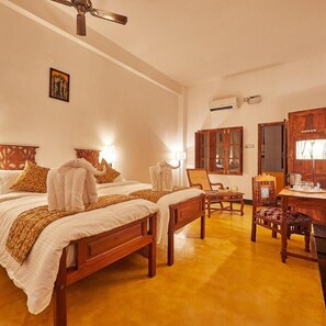 A hotel room with two wooden beds, a wooden chair, a small table, and a ceiling fan. - Villa Du Ocean (Puducherry)