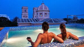 A couple relaxing by a pool with a view of a church with two towers and a dome. - Villa Du Ocean (Puducherry)