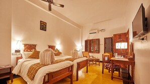 A hotel room with two beds, a desk, a chair, a ceiling fan, and a television. - Villa Du Ocean (Puducherry)