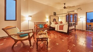 A four-poster bed with a canopy, a wooden chair with a woven seat, a small table with a magazine, and a floor with a floral pattern. - Villa Du Ocean (Puducherry)