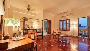 A spacious room with a wooden dining table, a four-poster bed, and a balcony with a view of the sea. - Villa Du Ocean (Puducherry)