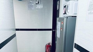 A narrow hallway with white and black tiled floors, a clock on the wall, a fire extinguisher, and a refrigerator. - New Cosmos Hotel (Kowloon)