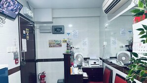 A small office with a desk, two chairs, a fire extinguisher, a trash bin, and a wall-mounted fan. - New Cosmos Hotel (Kowloon)