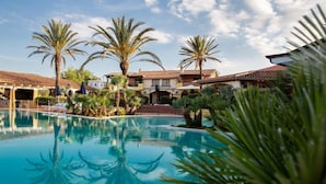 A pool area with palm trees and a building with a tiled roof. - TH San Teodoro Liscia Eldi Village (San Teodoro)