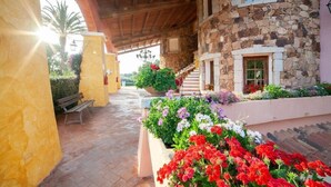 A stone building with a wooden staircase and a covered patio area with flower beds. - TH San Teodoro Liscia Eldi Village (San Teodoro)