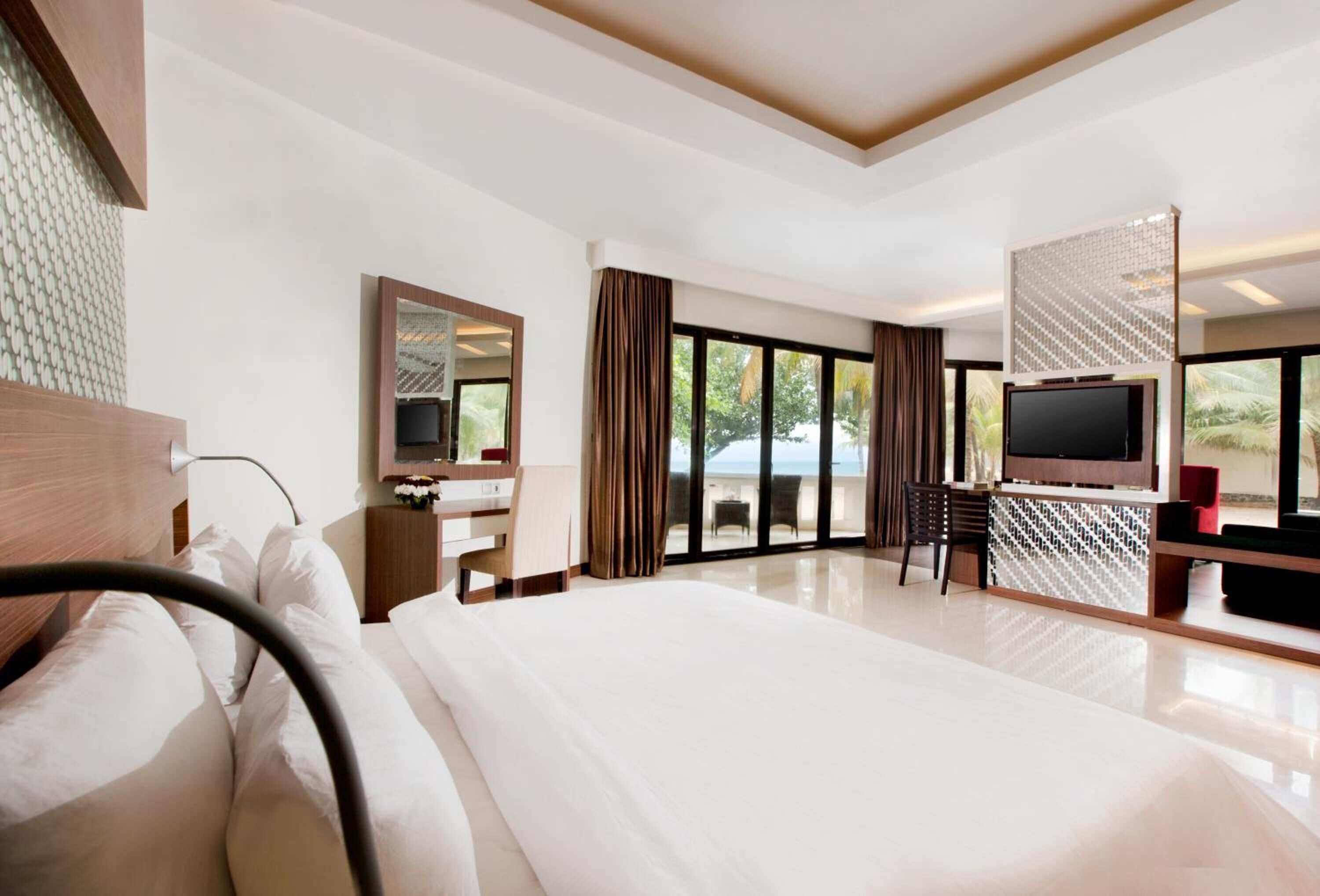 Quarto de hotel moderno com uma cama grande, uma mesa com computador, uma televisão e uma varanda com vista para o exterior.
