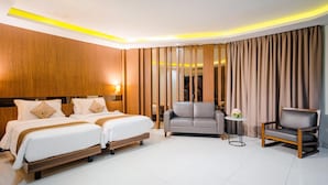 Ein Hotelzimmer mit zwei Betten, einem Schlafsofa, einem Sessel und einem kleinen Tisch.