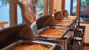 Ein Buffet mit verschiedenen Speisen, darunter ein Auflauf und ein Nudelgericht, in einem gut beleuchteten Raum mit einem großen Fenster und einem Baumstamm im Hintergrund.