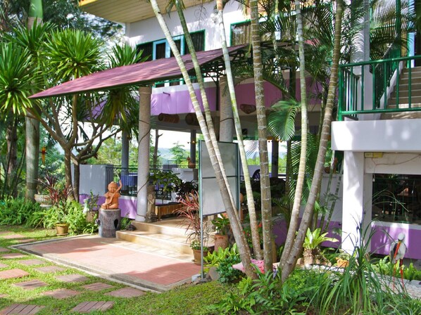 A tropical resort with a covered outdoor area, palm trees, and a statue. - Phucome Resort (Khao Kho)