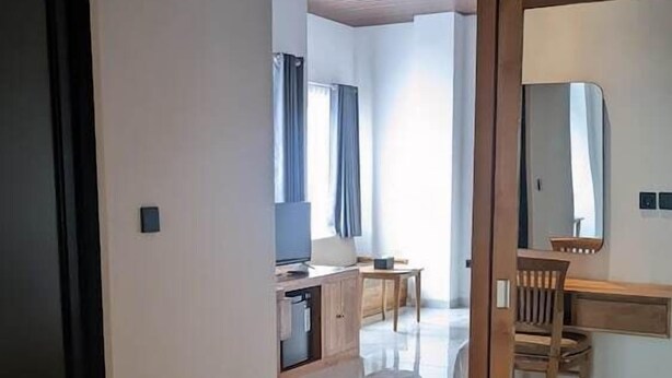 A modern hotel room with a large mirror, a wooden desk, a television, and a dining area with a chair and table. - Sujiwa Ubud Retreat (Sukawati)