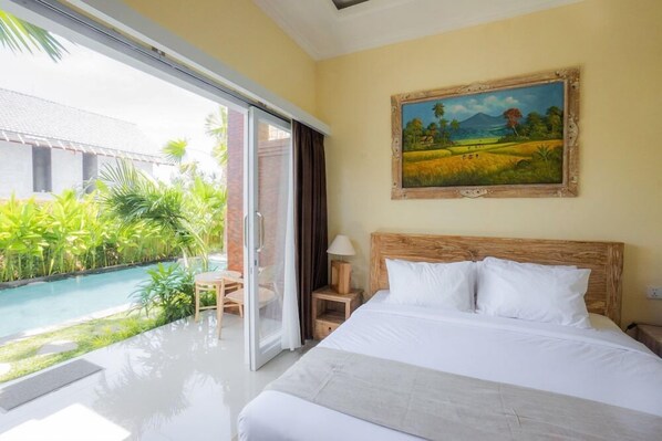 Hotelkamer met een bed, een schilderij, uitzicht op een zwembad en een deur naar een buitenruimte met planten.