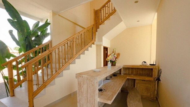 A staircase with wooden railings leading to an upper floor, a bench with a vase of flowers, and a plant near the staircase. - Sujiwa Ubud Retreat (Sukawati)