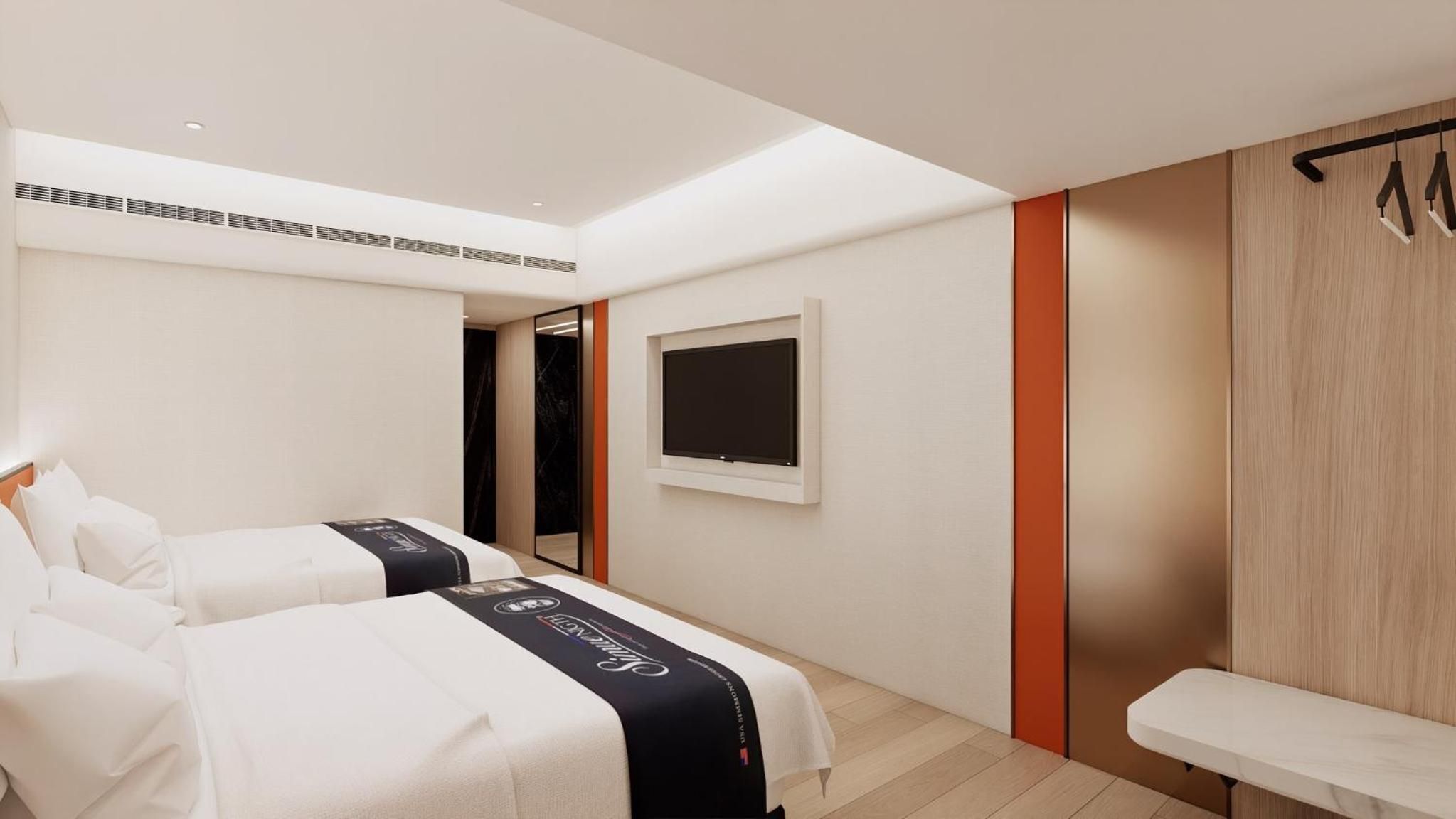 A hotel room with two beds, a TV mounted on the wall, a bench, and a wooden panel wall.
