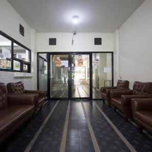 A reception area with a glass door, two brown leather sofas, a tiled floor, and a ceiling light. - Monta Apartment (Chonburi)