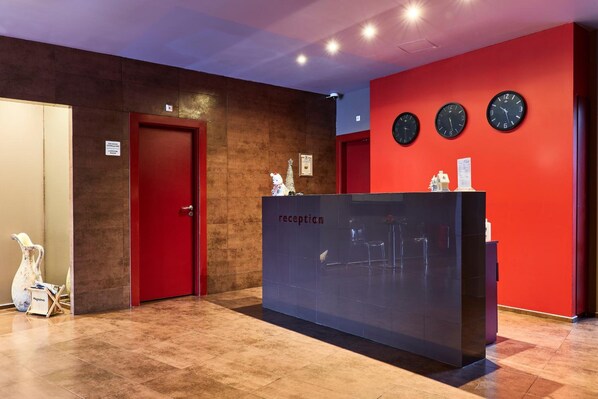 A reception area with a red wall, three clocks, and a reception desk. - Mirena Hotel (Plovdiv)