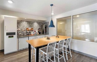 Una cocina moderna con una mesa de comedor de madera y sillas blancas, una lámpara colgante azul y un salpicadero decorativo.