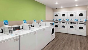 A laundry facility with multiple washing machines and dryers, a green wall, and a wooden floor. - Woodspring Suites Riverside Norco (Norco)