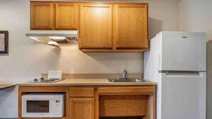 A compact kitchen with wooden cabinets, a microwave, a sink, and a refrigerator. - Woodspring Suites Riverside Norco (Norco)
